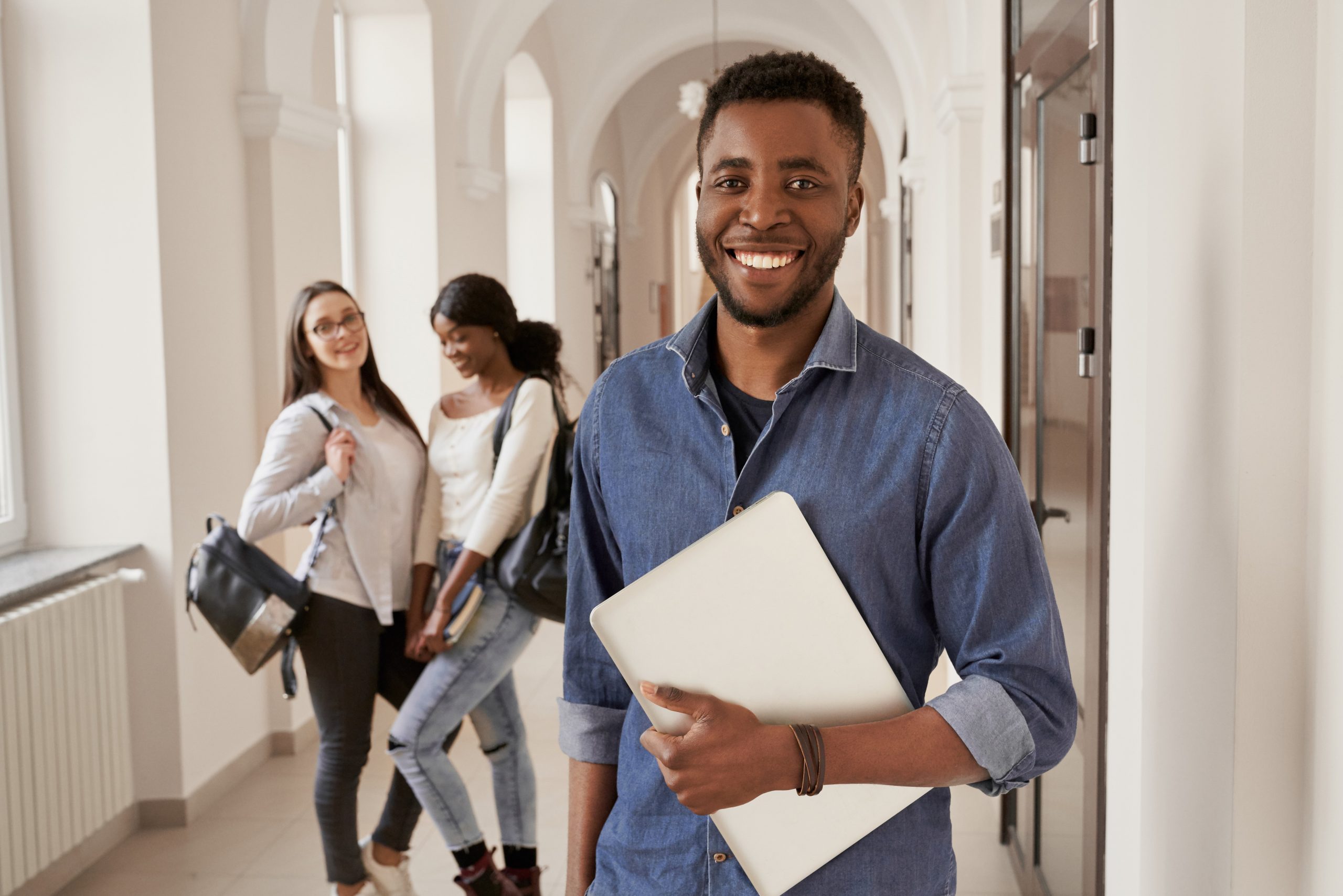 estudante universitário posa sorridente no corredor da universidade com colegas ao fundo